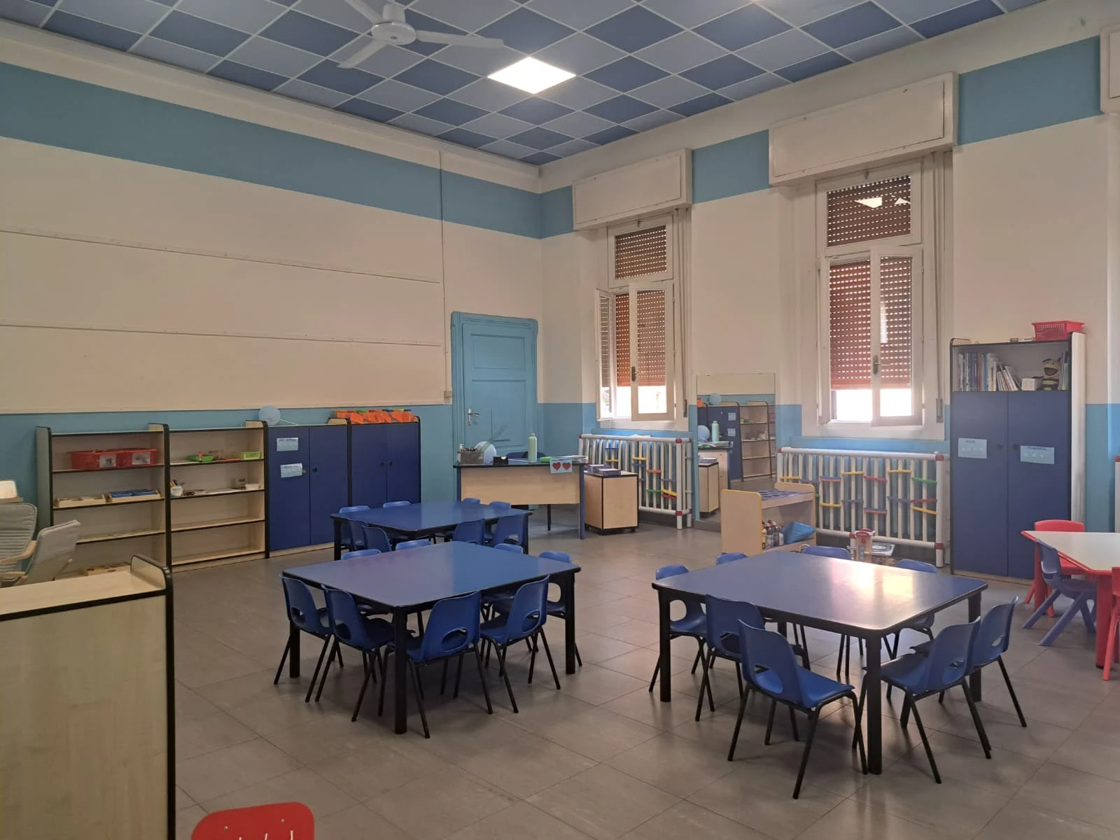Aula con tavolini blu e spazi per il gioco