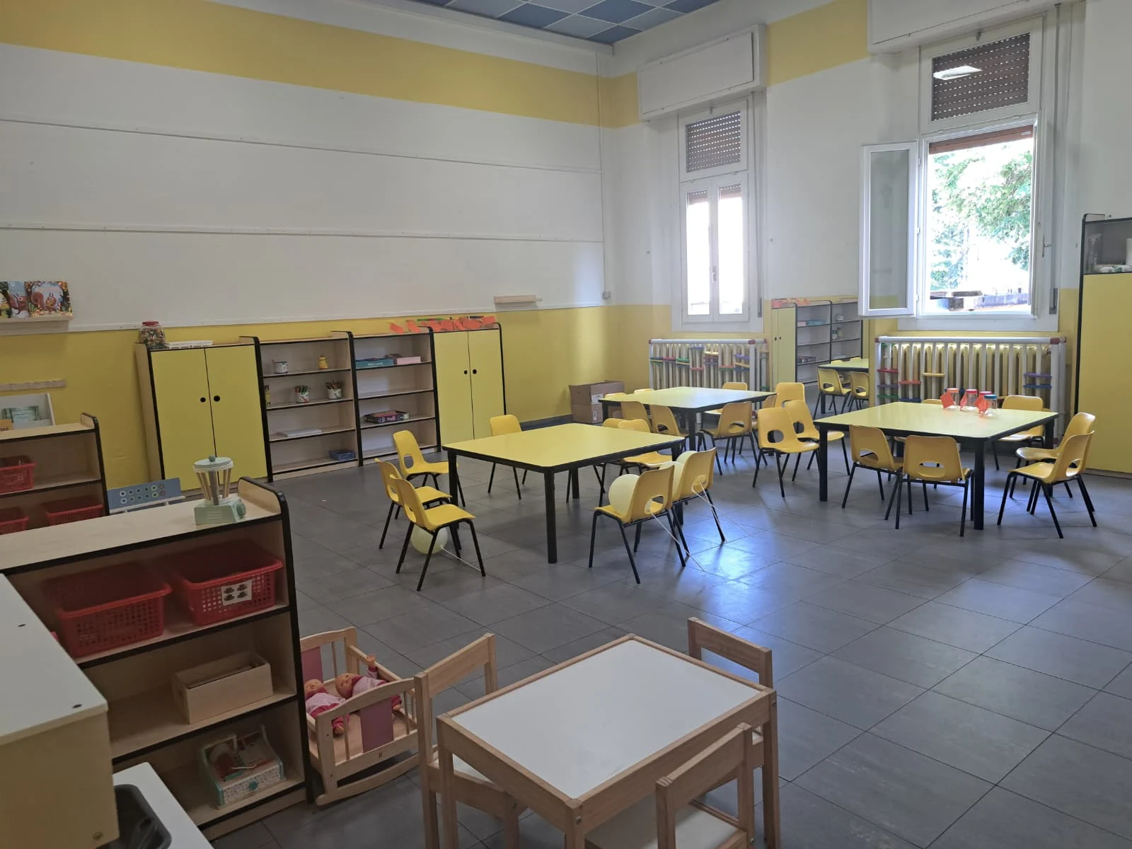 Aula con tavolini gialli e materiali didattici
